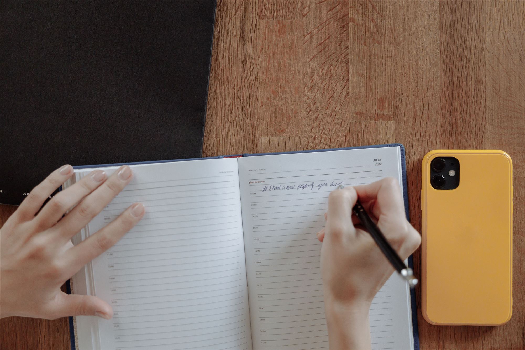 Hands writing the week's plan in a paper planner on a wooden desk